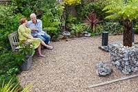 Bill and Bev Kerr in the most recently developed part of their garden. Planting includes Euphorbia mellifera, variegated bamboo, Dicksonia antarctica and castor oil plant - Ricinus communis in a galvanised metal container.