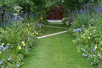 The Dog's Trust:' A Dog's Life', designed by Paul Hervey-Brookes. A stretch of lawn, criss-crossed by zig-zag paving. Plants include verbena bonariensis, agastache, angelica, cosmos, blue campanulas and geraniums and hemerocallis, with alchemilla mollis and erigeron karvinskianus. Hampton Court Flower Show July 2016