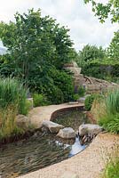 Rock stepping stones over a water rill, Cercidiphyllum japonicum with Prunus lusitanica and Panicum virgatum 'Northwind' -  Zoflora: Outstanding Natural Beauty, RHS Hampton Court Palace Flower Show 2016