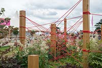 Persicaria polymorpha next to Oak posts with red cord tied, representing the Chinese myth called the Red Thread of FateThe Red Thread, Design: Robert Barker, RHS Hampton Court Palace Flower Show 2016