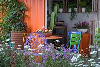 A sitting area with a view of a potting shed interior in the RHS Greening Grey Britain for Health, Happiness and Horticulture Garden. RHS Chelsea Flower Show 2016 - Designer: Annie-Marie Powell