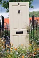 Cream painted front door surrounded by planting of Geum 'Fireball', Anthriscus sylvestris 'Ravenswing' and Stipa gigantea - The Modern Slavery Garden, RHS Chelsea Flower Show 2016, Design: Juliet Sargeant, Sponsor: The Modern Slavery Garden Campaign