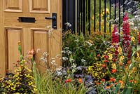 The Modern Slavery Garden, mixed colourful planting with open door and railings. RHS Chelsea Flower Show 2016. Designer: Juliet Sargeant - Sponsor: The Modern Slavery Garden Campaign - Contractor: The Outdoor Room