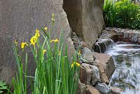 The M and G Garden, view of Forest of Dean stone water feature with Iris pseudacorus. RHS Chelsea Flower Show, 2016 Designer: Cleve West MSGD, Sponsor: M and G 
