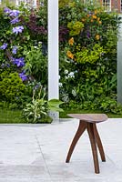 A traditional Japanese stool in front of  a living wall with Clematis 'Patensella' in The Watahan East and West Garden. The RHS Chelsea Flower Show 2016 - Designer: Chihori Shibayama and Yano Tea - Sponsor: Watahan - SILVER