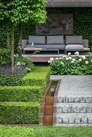Husqvarna Garden, the seating area with copper water rill and planting including  white Paeony 'Mother's Choice', espaliered Carpinus betulus, Buxus sempervirens topiary, Taxus bacatta hedge. The RHS Chelsea Flower Show 2016 