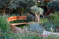 The Winton Beauty Of Mathematics Garden. Curving timber bench with Copper backing in garden with mediterranean style planting. The RHS Chelsea Flower Show 2016, Designer: Nick Bailey, Sponsor: Winton