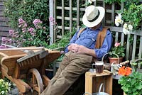 Middle aged gardener sleeping surrounded by garden tools and a glass of beer, Norfolk, Uk, June