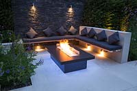 Secluded seating area with a dry stone slate wall and propane fire pit emitting blue light