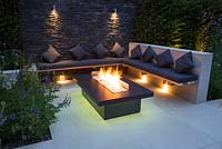 Secluded seating area with a dry stone slate wall and propane fire pit emitting yellow light