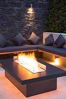 Secluded seating area with a dry stone slate wall and propane fire pit emitting orange light