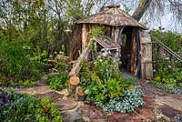 Wooden hut and log store with Ajuga, Lamium, Euphorbia and Heuchera - The Woodcutter's Garden, RHS Malvern Spring Festival 2016. Design: Mark Walker