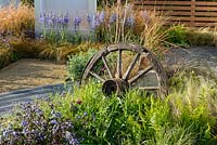 Old cart wheel surrounded with  Polystichum polyblepharum, Stipa tenuissima and Polemonium 'Heaven Scent', Carex testacea and Camassia in the background. The Low Line, RHS Malvern Spring Festival 2016. Design: Jamie Langlands