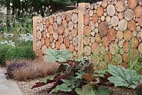 Boundary walls constructed from log slices and a gravel bed containing rheum, buxus and carex. The Perspective Garden, RHS Tatton Flower Show 2011, Cheshire