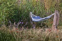 Stipa tenuissima and a hammock suspended from rough wooden posts. Garden: 'One Man Went To Mow' at RHS Tatton Park Flower Show 2012 