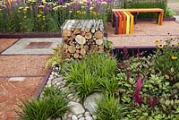 Multi coloured bench, mixed hard surfaces and gabions filled with logs. Garden: 'Nature Squared' at RHS Tatton Park Flower Show 2012