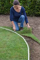 Using a knife to cut newly laid turf to shape, following along the rope guide