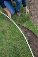 Using a knife to cut newly laid turf to shape, following along the rope guide