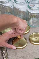 Using a bradle to create holes in the centre of the glass jar lids