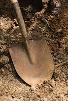 Close-up of old rusted metal digging shovel in dirt pit
