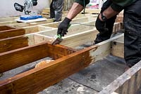 Applying wood preservative to joists before laying decking in small urban garden