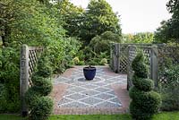 Jackie Healy's garden near Chepstow. Early autumn garden. Paved area with potted conifer and paired topiary Box bushes