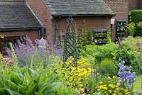 A cottage garden with metal obelisk and large mixed border of Nepeta, Oenothera, Campanula, Digitalis and Geranium.