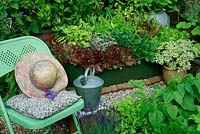 Mini kitchen garden with a tin bath planted with herbs and salad vegetables, dwarf beans, parsley and endive. A seat and watering pot provide focal points.