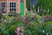 The Harrods British Eccentics Garden, RHS Chelsea Flower Show. A view of the octagonal folly, through a perennial border of hardy geranium, salvia, foxgloves, ragged robin and roses. Designer: Diarmuid Gavin. Sponsor: Harrods.