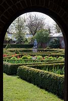 A view into a walled formal garden with box parterres filled with spring bulbs.
