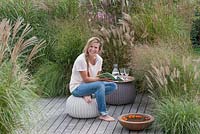 Woman relaxing on deck. Border with grasses - Pennisetum, Miscanthus and Panicum 