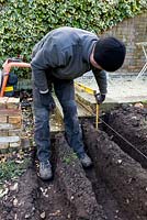Construction of stepped border in London garden - the first foundation trenches being dug, with the builder measuring depth