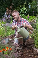 A man using a watering can to water Nasturtiums in a border