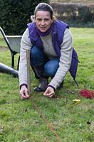 A woman using stakes and string to create a guide outline for the base of the arbour 