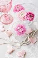 Pink Ranunculus in glass containers in an arrangement with hearts and pearls