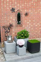 Arrangement of contemporary rattan planters on hardwood decking by wall of suburban house with mirror and metal artwork