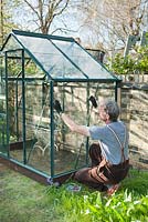 Man inserting glass pane into place - wearing protective gloves. The top pane of glass sits on small metal' z' clips: April, Spring.