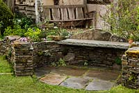 Curved stone wall seating area with weathered oak bench beyond - Macmillan Legacy Garden - RHS Malvern Spring Show 2016. Designer: Mark Eveleigh, Sponsor: Macmillan Cancer Support