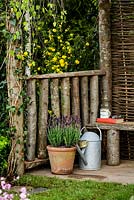 Edge of timber seating area with terracotta pot and metal watering can - The Water Spout garden - RHS Malvern Spring Show 2016. Designer: Christian Dowle. Sponsor: Garden Inspiration