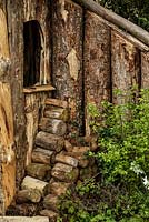 Edge of rustic wooden hut with stacked log pile - The Woodcutter's Garden - RHS Malvern Spring Show 2016. Designer: Mark Walker, Sponsor: Howards Motors
