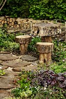 Stepping stones, table and stools made from tree trunks surrounded by woodland planting - The Woodcutter's Garden - RHS Malvern Spring Show 2016. Designer: Mark Walker, Sponsor: Howards Motors