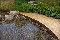 Stream with slate base layered at 90 degree angle. Steel edged with gravel path bordered by ferns and grasses. Zoflora - Outstanding Natural Beauty Garden, RHS Hampton Court Flower Show, 2016. 