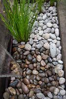 Juncus effusus planted among pebbles by water feature. Railway sleeper garden divider. Fancy a brew - Take a pew. RHS Hampton Court Flower Show, 2016. 