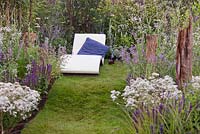 A lounger provides a place to relax on an undulating strip of lawn between purple, blue and white flower beds - July, 'Surf 'n' Turf' at RHS Tatton Flower Show 2015
