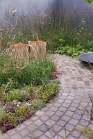 A naturalistic planting of grasses and perennials enclose a stone cobbled seating area with shallow water bowl - July, 'A Quiet Corner' at RHS Tatton Flower Show 2015
