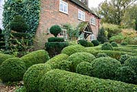 Front garden contains a plump box parterre punctuated by vertical yew topiary.