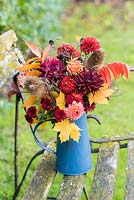 Autumn flower arrangement with Dahlias, autumn leaves, seedheads and chrysanthemums in blue jug