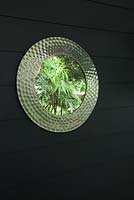 Patterned mirror on wall reflecting green garden foliage