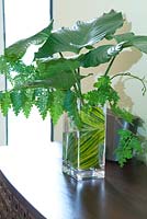 Vase displaying an assortment of leafy foliage sits on timber table 