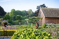 View from terrace: border of perennials, child angel statue, gardenhouse and decorative urn. Yvan and Gert garden In Belgium.